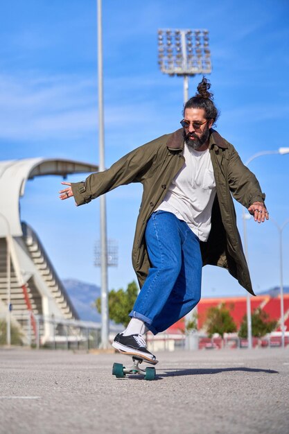 Positive adult stylish dressed man riding skateboard in\
park