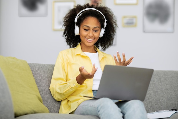 Positive african american woman holding video conference on\
laptop, sitting at home, talking and ges