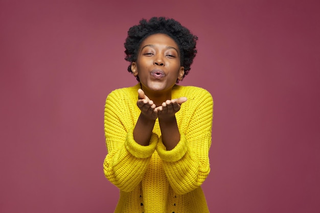 Positive african american young woman with curly afro hair blowing kiss farewell gesture feeling