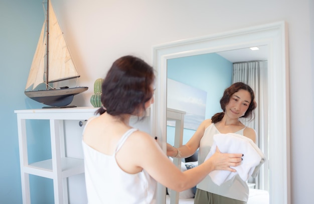 Positive asian woman housewife tidying modern home happy woman\
doing domestic chores asian housewife wiping shelf furniture bed\
mirror sofa and home appliances