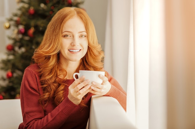 Photo positive attitude to life. smiling woman of heavenly beauty relaxing on a sofa and enjoying her cup of warm tea on a christmas morning.