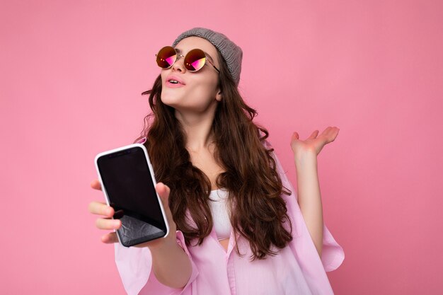 Positive attractive young brunette female person wearing stylish pink shirt grey hat and colourful