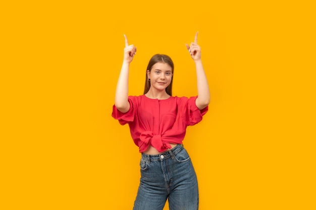 Positive attractive young woman shows something up in empty space isolated on bright yellow background