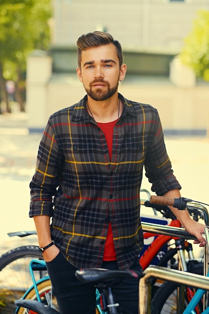 양털 셔츠를 입은 긍정적인 수염 난 남성이 자전거 주차장 근처에 있습니다.
