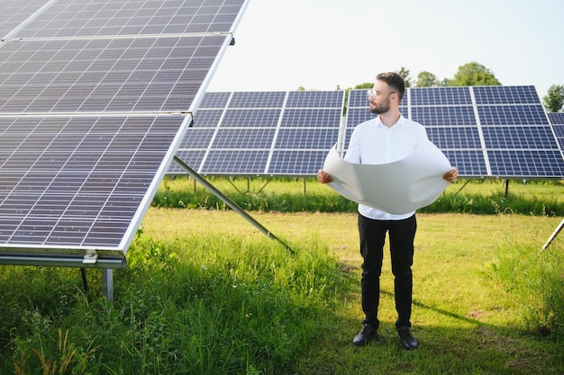 Positive bearded male investor standing against photovoltaic panels producing alternative energy