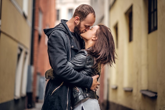 Positive bearded male kissing cute brunette female on a street in an old town.