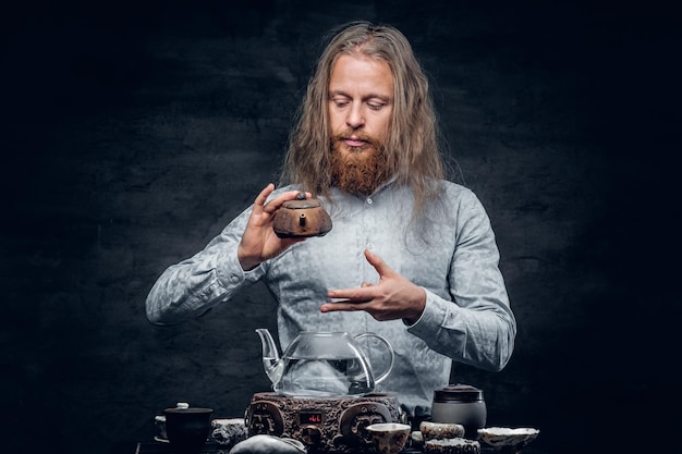 Positive bearded male pours hot water in a tea ceremony.