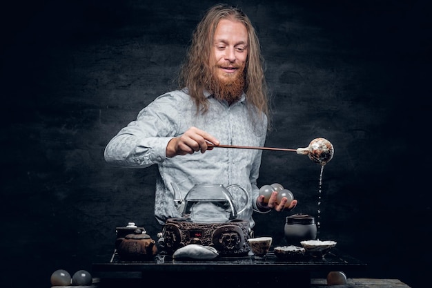 Positive bearded male pours hot water in a tea ceremony.