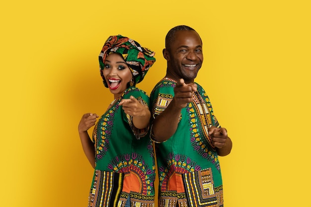 Positive black couple in african costumes pointing at camera