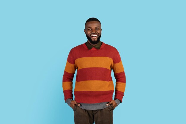 Positive black man standing with hands in pockets and smiling at camera