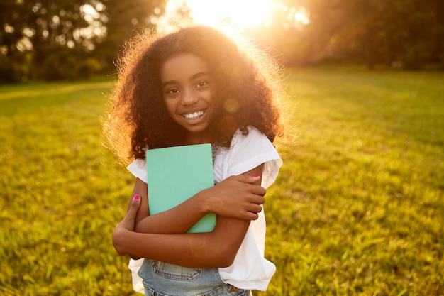 Positive black schoolgirl with textbook in park