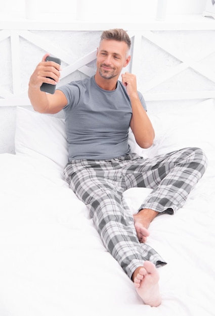 Foto uomo di blogging positivo con il telefono indossa il pigiama uomo di blogging con il telefono a letto