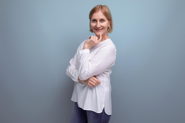 Positive blond middle aged woman in white blouse on studio background