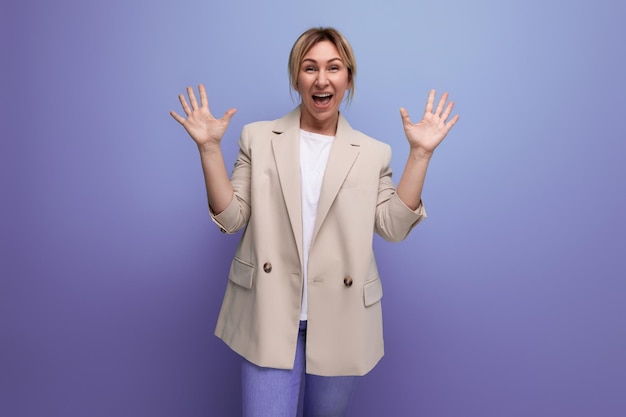 Positive blond young business woman in jacket smiling on studio background