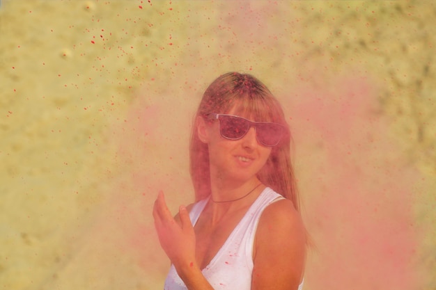 Foto ragazza bionda positiva in occhiali da sole che gioca con vernice secca colorata holi al deserto. spazio vuoto