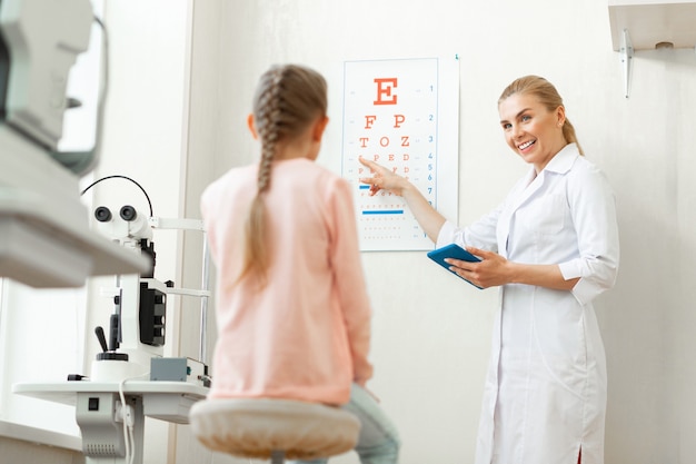 Photo positive blonde oculist in white robe pointing on a red letter