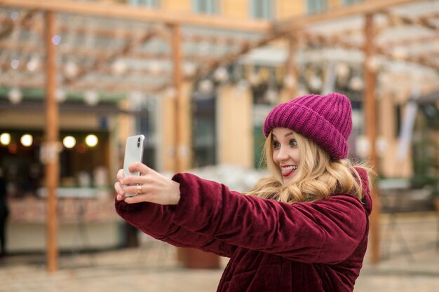 Positive blonde woman having fun and making self portrait at the background of garland in Kiev