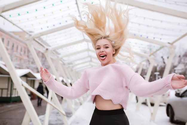 Positive blonde woman with long hair in motion jumping at the street