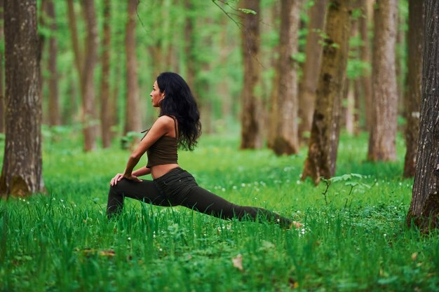 Foto bruna positiva che fa fitness all'aperto nella foresta durante il giorno