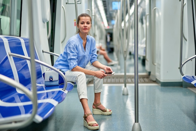 Положительная девушка брюнет с помощью мобильного телефона в метро.
