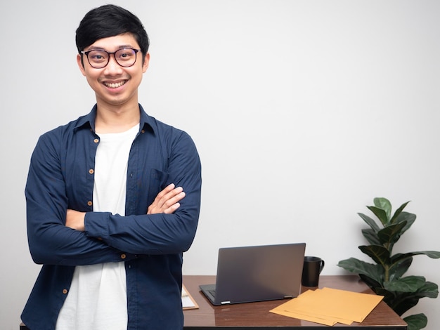 Positive businessman glasses smile stand cross arms at workplace room copy space