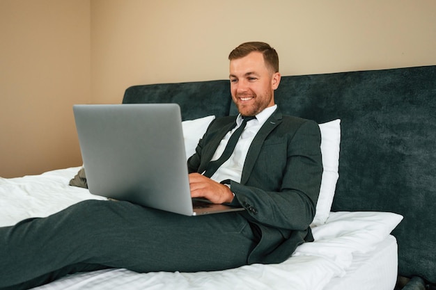 Positive businessman is indoors in the hotel room using laptop