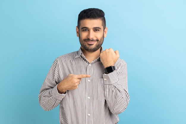 Positive businessman with beard pointing at wristwatch on hand and smiling showing new smart clock