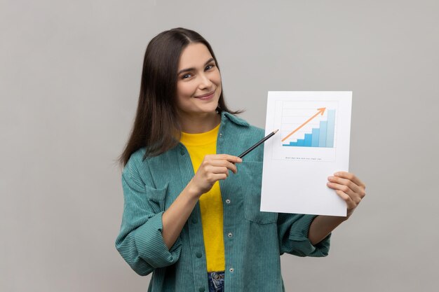 Positive businesswoman holding paper chart showing increase of workers salaries pointing to paper