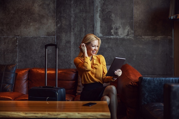 Positive businesswoman sitting in a hall of a hotel and checking in a hotel online. She is on a business trip. Telecommunications, travel, business trip