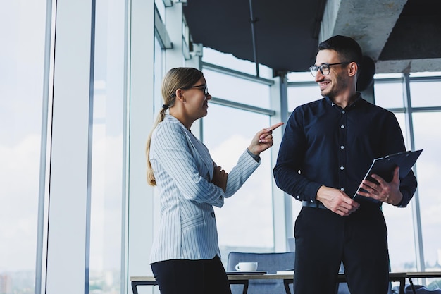 Positive businesswoman standing with Caucasian male colleague talking to businessman in office Business relations between colleagues with smiles in a warm atmosphere