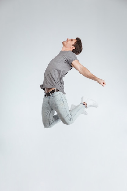 Positive carefree casual young man jumping in the air isolated on a white background