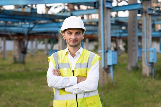 Positive caucasian adult worker engineer in helmet smiling at camera at high voltage power station