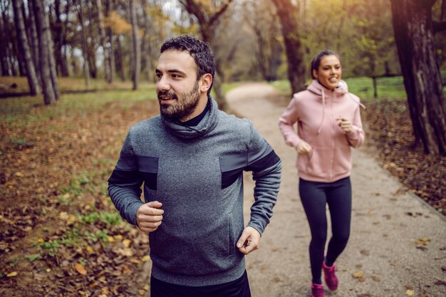 Positive caucasian bearded sportsman running in nature with his girlfriend.