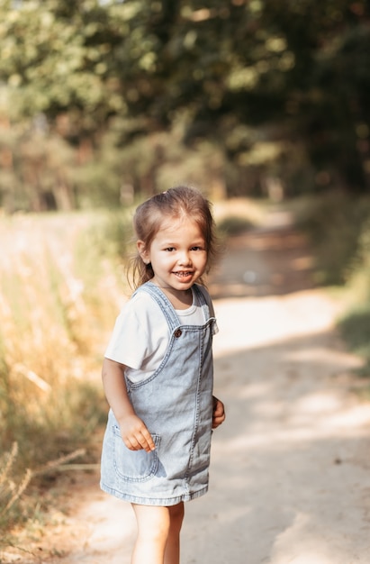 Bambina affascinante e positiva che si gode la giornata di sole estivo, le emozioni dell'espressione, il divertimento, il bambino felice che cammina nella giornata estiva