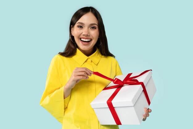 Positive cheerful young brunette lady holding wrapped gift box