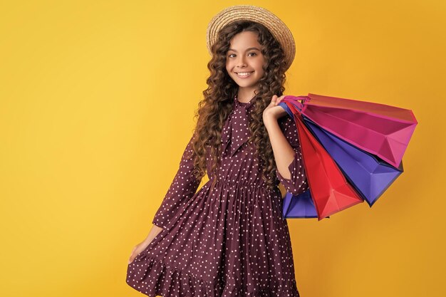 Photo positive child with curly hair hold shopping bags on yellow background