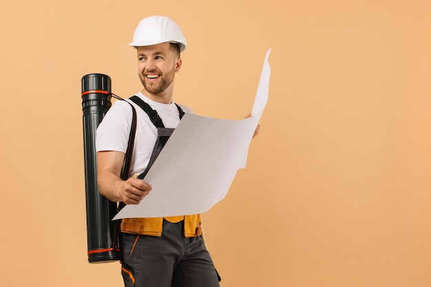 Positive construction engineer examines a drawing and holds a tube on a beige background