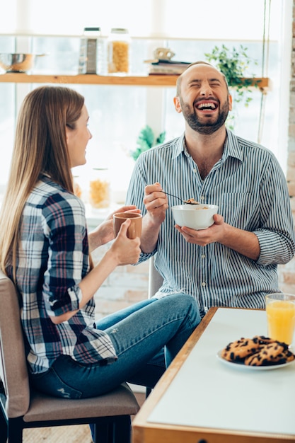 家で朝食をとっているポジティブなカップル。笑って目を閉じてボウルで面白がって男