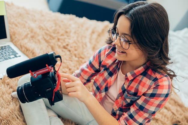 Positive creative girl changing settings in her camera while
preparing it for recording video with a microphone switched on