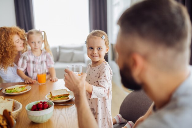 Positive cute girl giving a glass of juice to her dad