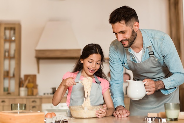 ポジティブなお父さんとプレティーンの女の子がボウルで材料を混ぜ、キッチンでクッキーの生地を作る