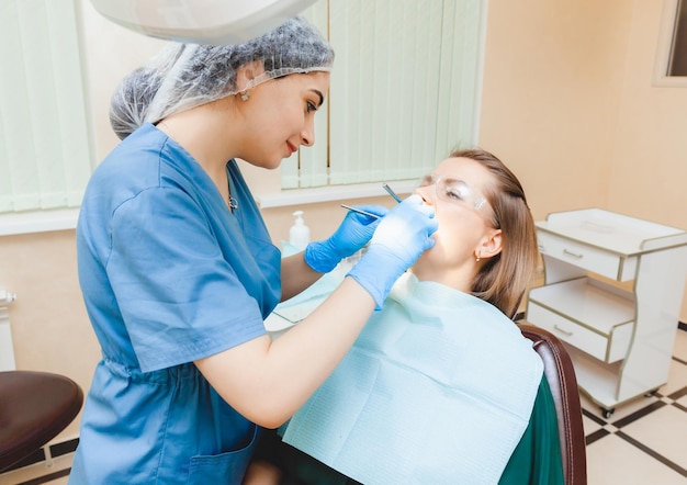 Позитивная темноволосая женщина сидит в кабинете стоматолога во время осмотра стоматолога, осматривающего женские зубы
