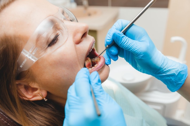 A positive darkhaired woman sits in the dentist's office during a checkup dentist examining woman's teeth