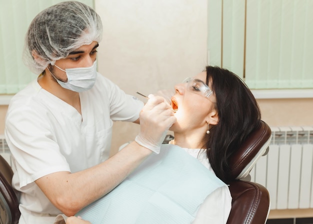 A positive darkhaired woman sits in the dentist's office during a checkup dentist examining woman's teeth