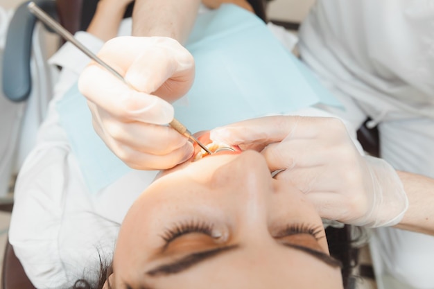 A positive darkhaired woman sits in the dentist's office during a checkup dentist examining woman's teeth