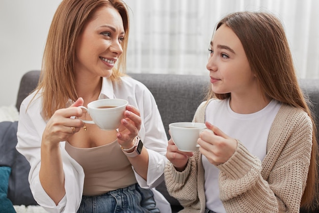 Positive daughter and mother drinking tea at home