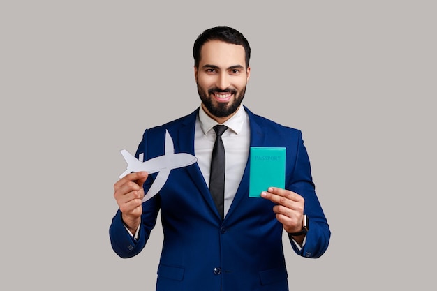 Positive delighted bearded man smiling and showing passport and paper airplane at camera tourism