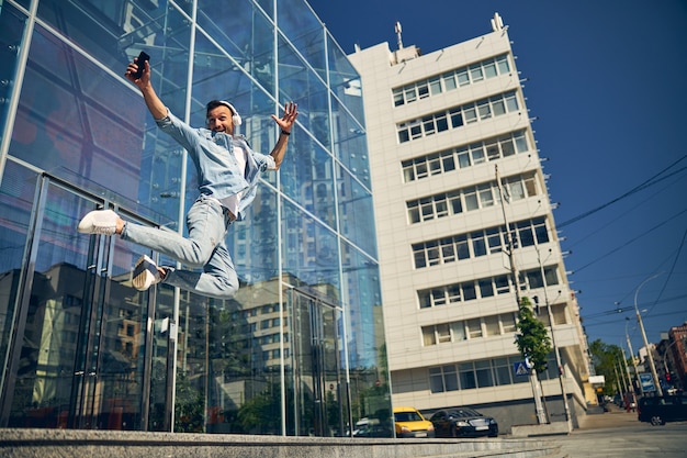 Positive delighted man wearing headphones and listening to music while posing on camera