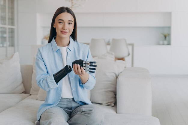 Positive disabled young woman is disassembling bionic arm prosthesis and smiling