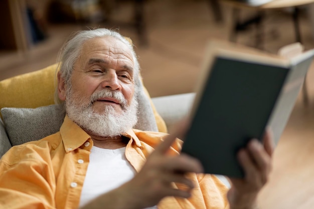 Positive elderly man laying on couch reading book